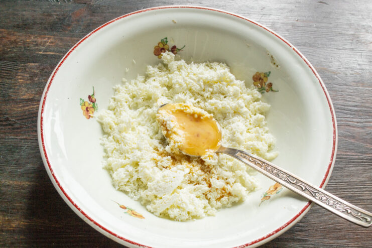 Preparing the Egg for the Syrniki Dough - Whisking the egg lightly. A raw egg in a small glass bowl being whisked with a fork.
