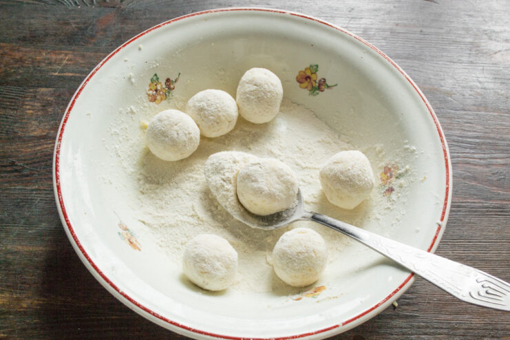 Dredging Syrniki in Flour - Creating a perfect crust for frying. Syrniki dough balls being rolled in a bowl of flour to get an even coating.