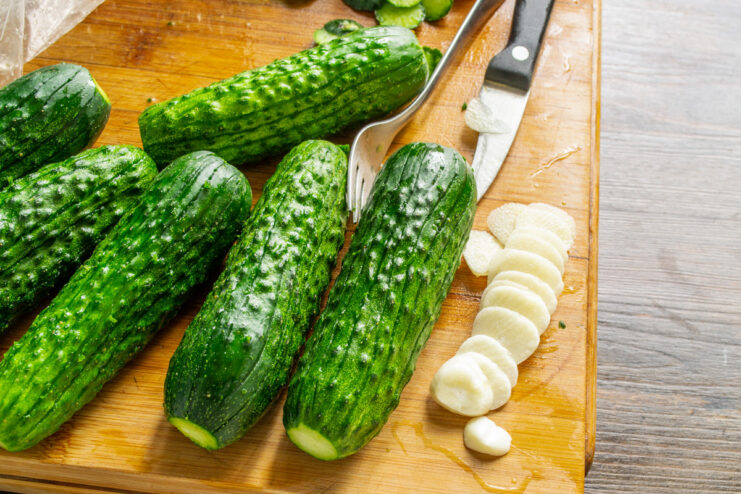 Thinly sliced garlic releases its flavor perfectly into the pickles. Close-up of a hand slicing a garlic clove into thin slices with a sharp knife.