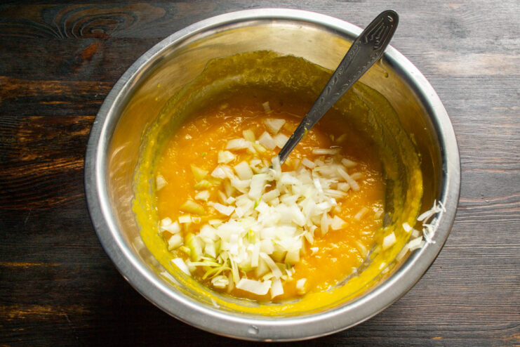 Incorporating Chopped Onion for Savory Flavor. Finely dice the onion for even distribution. Finely chopped onion being added to the pumpkin and egg mixture in a bowl.