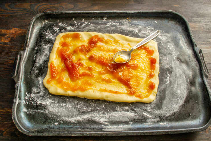 Spreading apricot jam over the cookie dough base Spreading a layer of apricot jam over the rectangular cookie dough.
