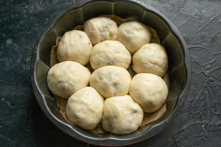 Letting the buns rise in a warm environment before baking A baking pan with arranged dough buns covered with a plastic bag for proofing.