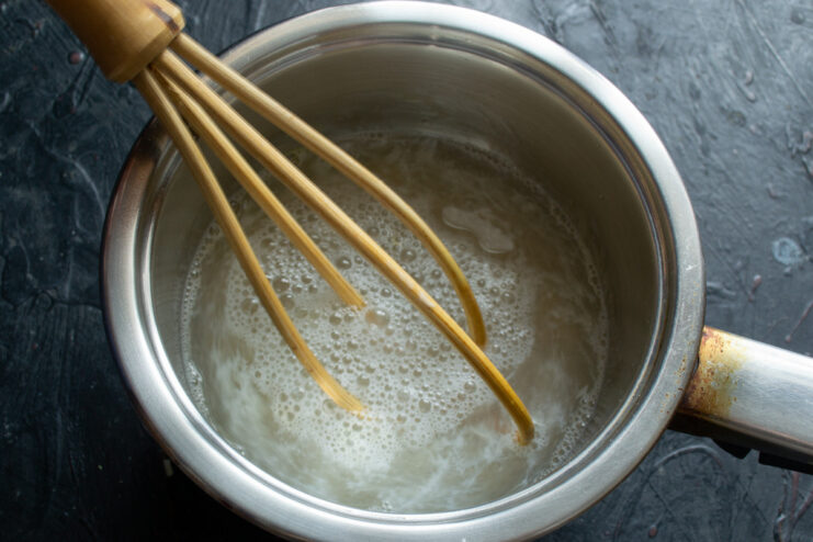 Activating the yeast: preparing the warm sugar-salt water A glass of water with sugar and salt being stirred.