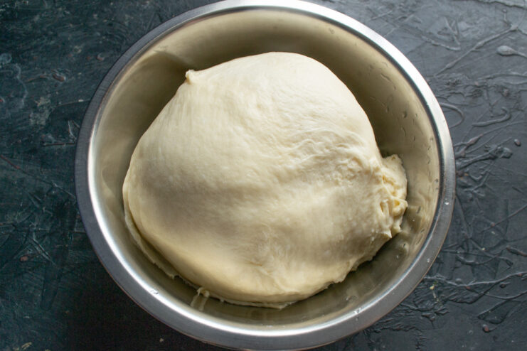 Kneading the dough until it's smooth and elastic A ball of dough being kneaded by hand on a floured wooden surface.