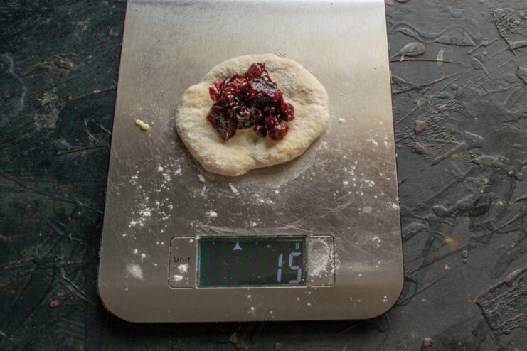 Filling each dough piece with a spoonful of jam A small, flattened piece of dough being filled with jam before being sealed.