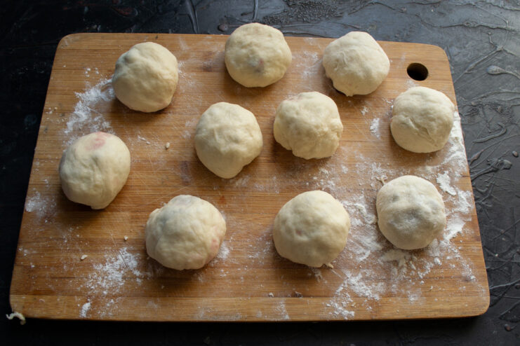 Shaping the jam-filled dough into perfect round buns Several small, round, uncooked dough buns filled with jam arranged on a surface.