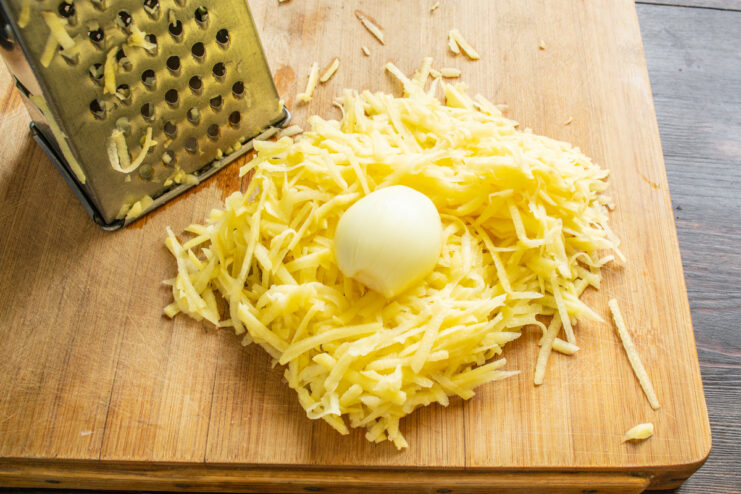 Adding Grated Onion to the Potato Mixture Grated onion being added to a bowl of grated potatoes for the fritter batter.