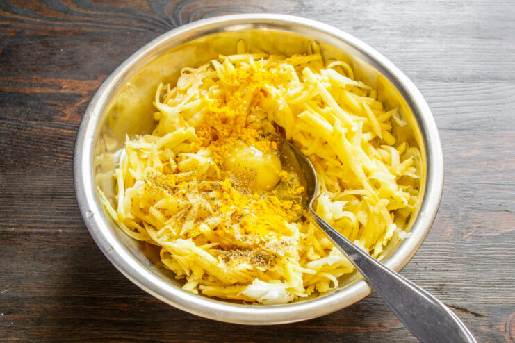 Seasoning the Fritter Batter with Spices Adding ground turmeric and black pepper to the vegetable fritter mixture in a bowl.