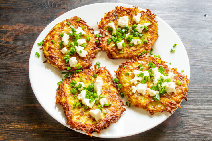 Serving Hot Vegetable Fritters with Toppings Ready-to-eat vegetable fritters on a plate, garnished with brynza cheese and green onions.