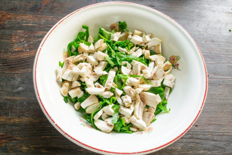 Adding Finely Chopped Mushrooms to the Spinach Adding chopped champignons to the bowl with spinach.