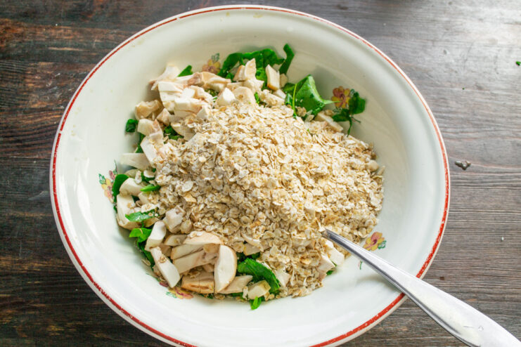 Adding Quick-Cooking Oats to the Mixture Pouring quick-cooking rolled oats into the bowl with vegetables.