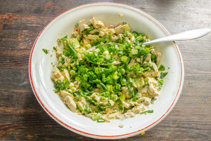 Adding Freshly Chopped Green Onions for Extra Flavor Adding chopped green onions to the mixture in the bowl.