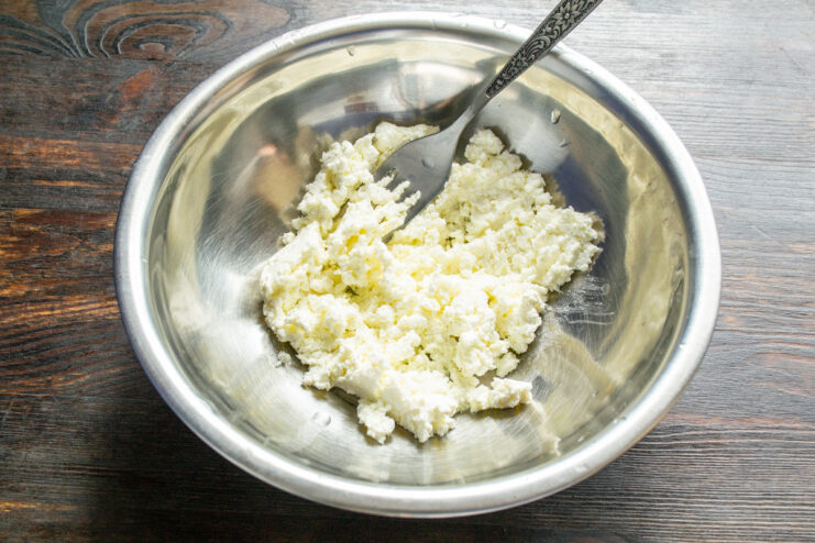Starting the cookie dough by adding tvorog (farmer's cheese) to a mixing bowl. A white bowl with a portion of tvorog (farmer's cheese) in it, the first step of the recipe.