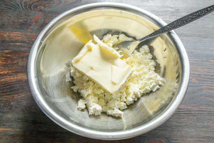 Combining softened butter with tvorog to create a creamy base for the cookie dough. Softened butter being added to a bowl of tvorog, ready to be mixed.