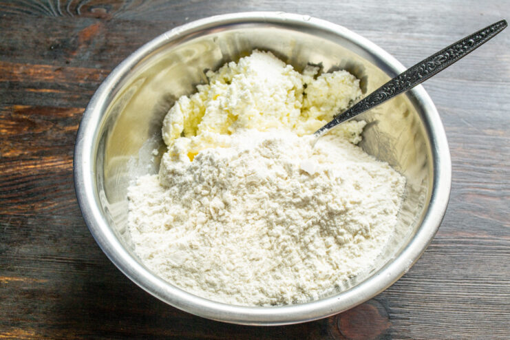 Combining wet and dry ingredients to form the tvorog cookie dough. Dry flour mixture being poured into the bowl with the creamed tvorog and butter.