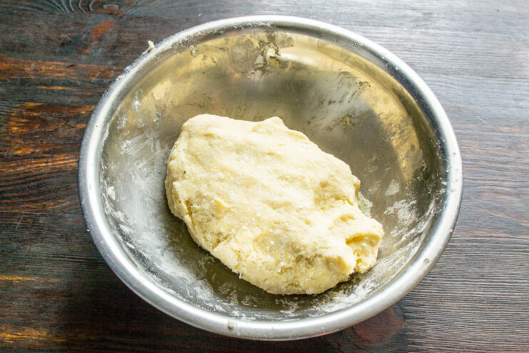 Kneading the dough until just combined to keep the cookies tender. Hands mixing the ingredients in a bowl to form a soft tvorog cookie dough.
