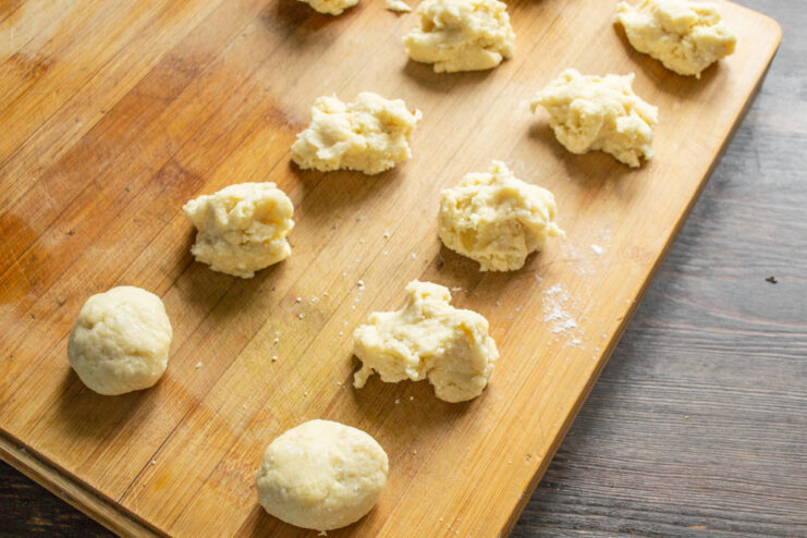 Portioning the chilled cookie dough for even baking. Chilled cookie dough divided into small, equal-sized balls on a wooden board.