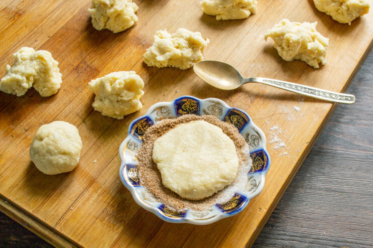Coating one side of the cookie dough with a generous layer of cinnamon sugar. A flattened circle of cookie dough being dipped into a cinnamon-sugar mixture.