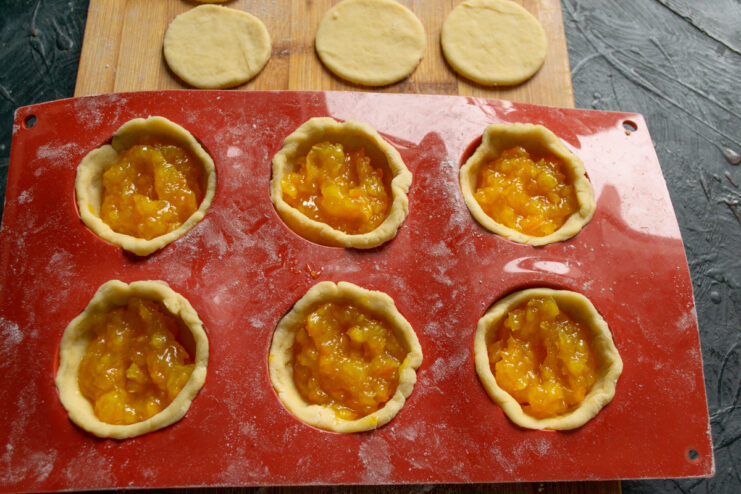 Filling the Cookie Cups with Homemade Marmalade Spoonfuls of orange marmalade being added to the dough-lined molds.