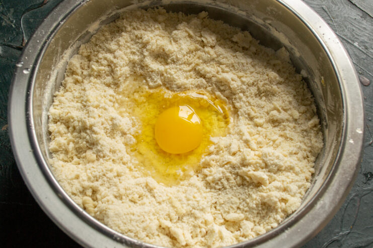 Adding an Egg to Bind the Cookie Dough An egg being added to the flour and butter mixture.