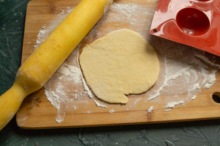 Rolling Out the Chilled Cookie Dough A piece of dough being rolled out thinly with a rolling pin on a floured surface.