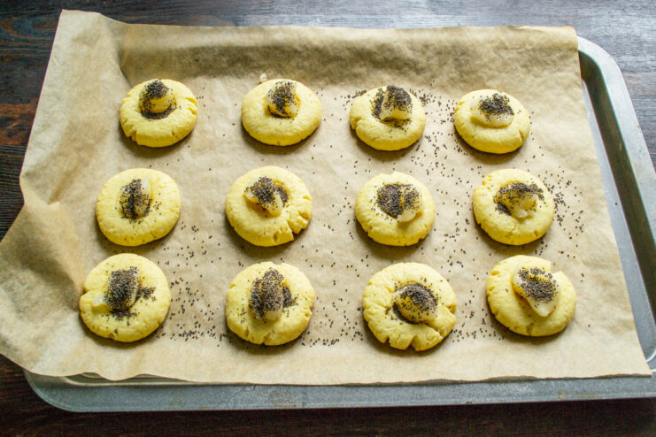 Topping the honey with poppy seeds for flavor and texture. Sprinkling poppy seeds over the honey-filled centers of the cookies.