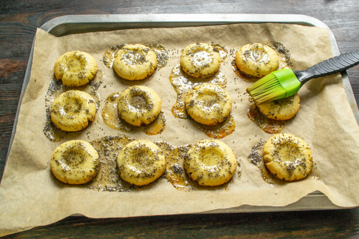 Glazing the cookies with melted honey and poppy seeds for a beautiful finish. Using a pastry brush to glaze the warm cookies with a honey and poppy seed mixture.