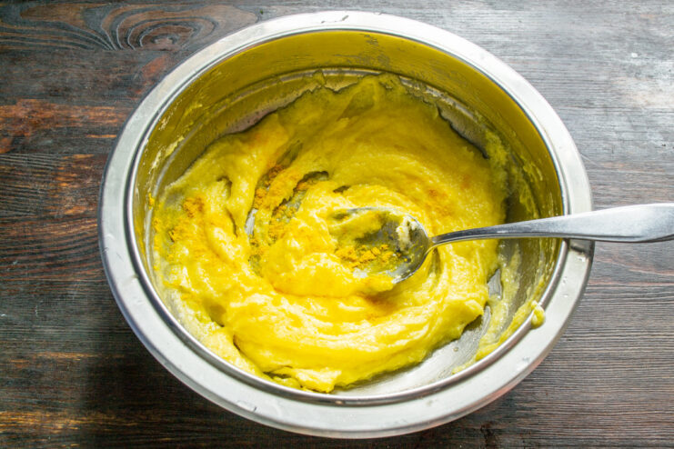 Whipping the wet ingredients until smooth and golden. Creamed butter, sugar, and egg yolks in a bowl with a pinch of turmeric.