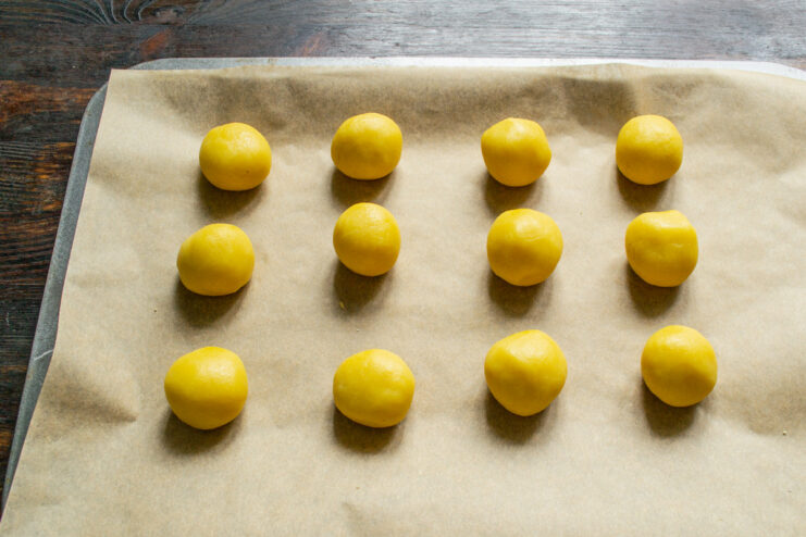 Portioning the cookie dough into small balls for even baking. Small, uniform balls of cookie dough arranged on a kitchen surface.