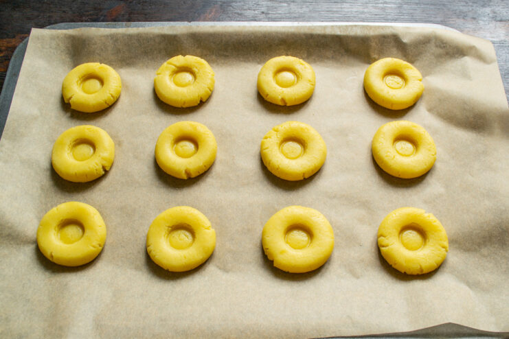 Shaping the cookies before making the indentations. Flattening balls of cookie dough into discs on a parchment-lined baking sheet.