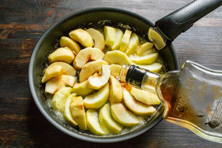 Adding a Rich Chocolate Liqueur Flavor to the Apples Pouring dark chocolate liqueur over apple slices cooking in a skillet.