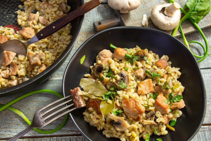 A bowl of pearl barley with meat and mushrooms, garnished with fresh parsley.