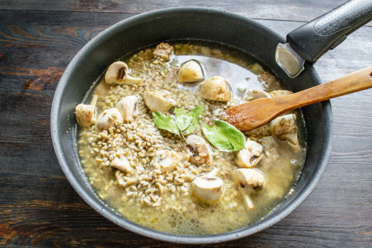 Pouring boiling water to cover the ingredients. Boiling water being poured into the pan, covering the pearl barley and other ingredients.