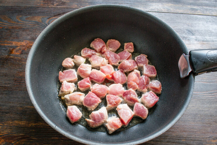 Searing the pork pieces in hot oil until golden brown. Pork cubes searing in a hot pan with oil.