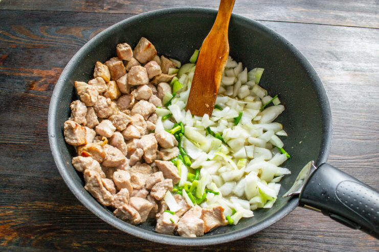 Cooking the meat and onions together in a large pan. Searing pork and chopped onions together in a large pan.