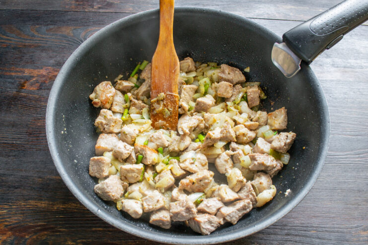 Sautéing the meat and onions until the onions are translucent. A close-up of pork and onions being cooked in a pan, with the onions becoming translucent.