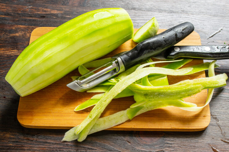 Step 1: Preparing the Zucchini for the Pizza Crust A hand peeling a green zucchini with a vegetable peeler over a cutting board.