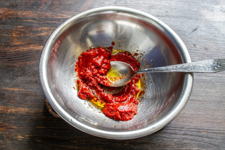 Preparing a Simple Tomato Sauce for the Pizza A small bowl with tomato paste and olive oil being mixed for the pizza sauce.