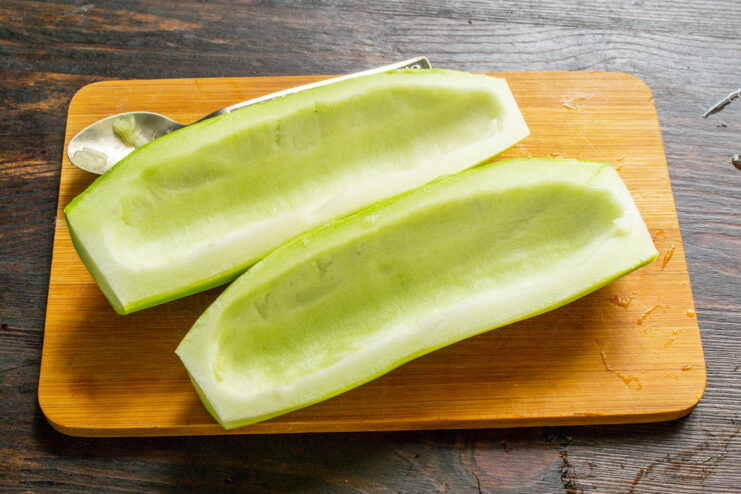 Removing Zucchini Seeds for a Firmer Pizza Base A spoon scooping out the seeds and pulp from a halved zucchini.