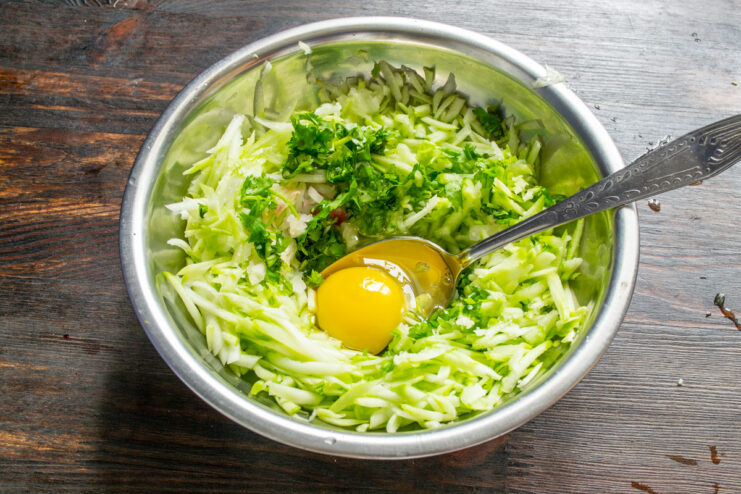 Mixing the Zucchini Base with Onion and Parsley A bowl with grated zucchini, chopped onions, and fresh parsley being mixed.