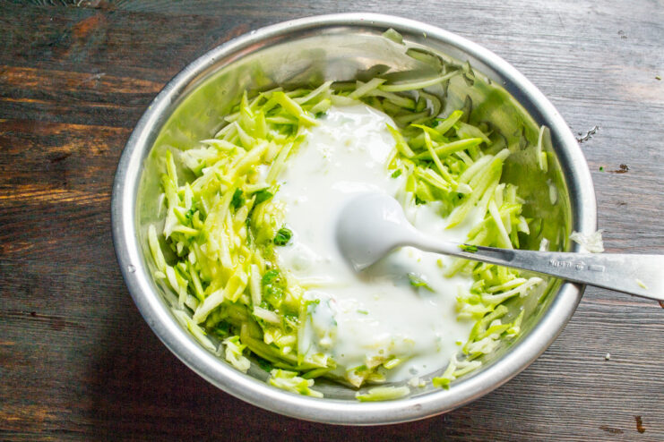 Adding Kefir to the Zucchini Mixture for Tenderness Pouring kefir from a glass into a bowl with the zucchini mixture.
