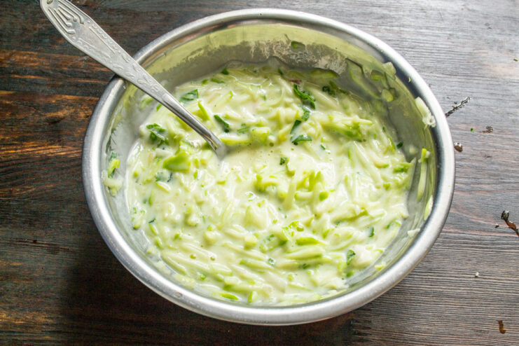 Combining All Ingredients for the Zucchini Pizza Dough A spoon mixing the zucchini, onion, parsley, egg, and kefir in a bowl.