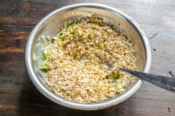 Adding Oats and Baking Soda to Thicken the Batter Adding quick-cooking rolled oats and baking soda to the zucchini batter in a bowl.