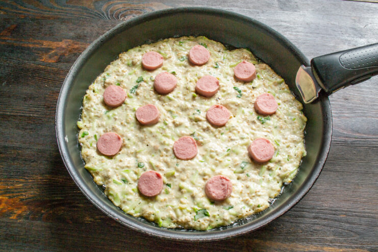 Adding Sausage Toppings to the Zucchini Pizza Placing sliced sausages on top of the uncooked zucchini crust in a skillet.