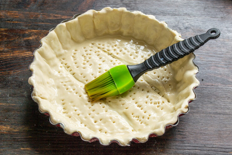 Applying Egg Wash to the Pastry - Brushing the dough with an egg and milk mixture for a golden finish. Brushing the raw puff pastry crust in a pan with an egg wash using a silicone brush.