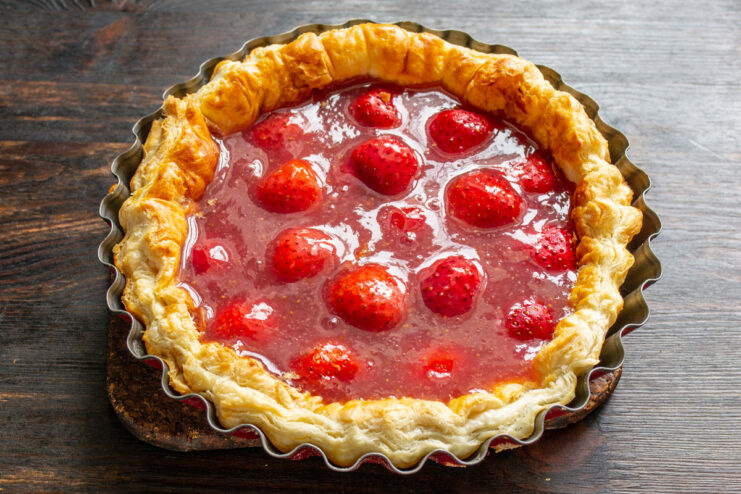 Pouring the Gelatin Filling Over the Strawberries - This will set to create a beautiful, glossy topping. Pouring the liquid strawberry and gelatin filling over the arranged strawberry halves in the pie crust.