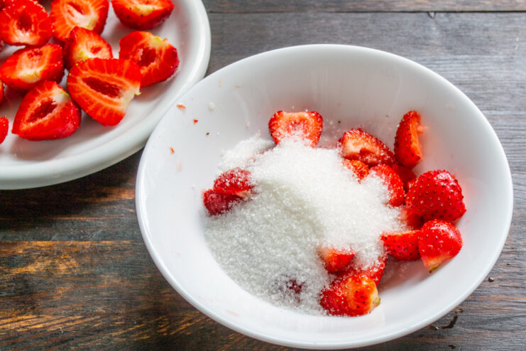 Adding Sugar to the Chopped Strawberries - Sweetening the base for the pie filling. Adding a spoonful of white sugar to a bowl of chopped fresh strawberries.