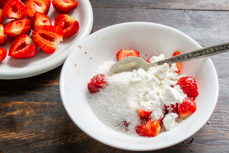 Adding Starch to Thicken the Strawberry Filling - A key step for a perfect pie consistency. Adding a spoonful of starch to the bowl of strawberries and sugar.