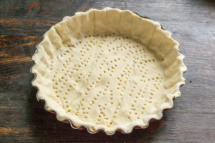 Docking the Pastry Base with a Fork - This prevents the dough from puffing up too much while baking. Docking the puff pastry base in a baking pan with a fork.