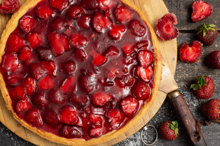 A whole strawberry pie with shortcrust pastry, topped with a glossy strawberry jelly filling, on a serving plate.